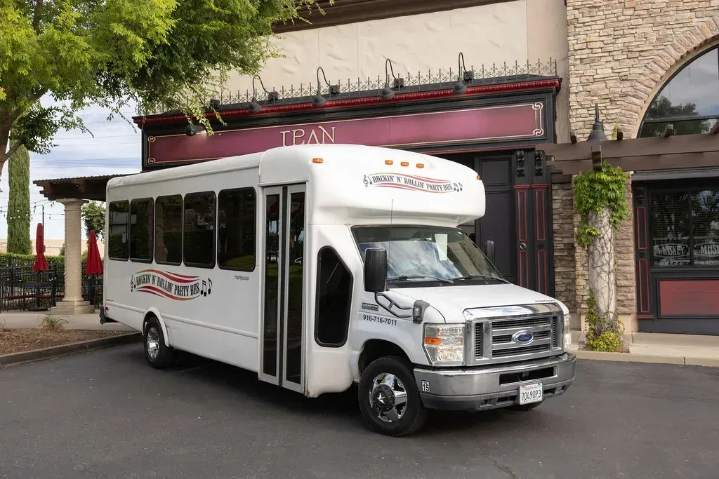 White shuttle bus parked outside a building with stone arches and a maroon awning