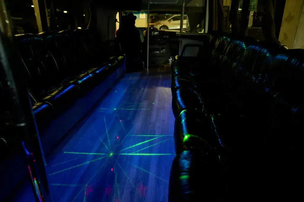 Empty bus interior with blue neon lighting and glowing floor panels, seen from the aisle.