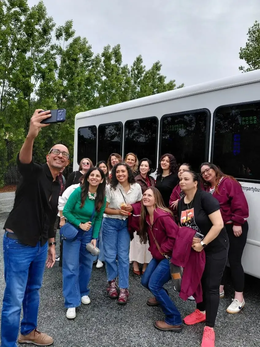 Group posing outdoors beside a white bus, with a small dog in front.