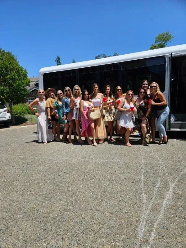 Group of people posing outdoors in front of a white bus on a sunny day.