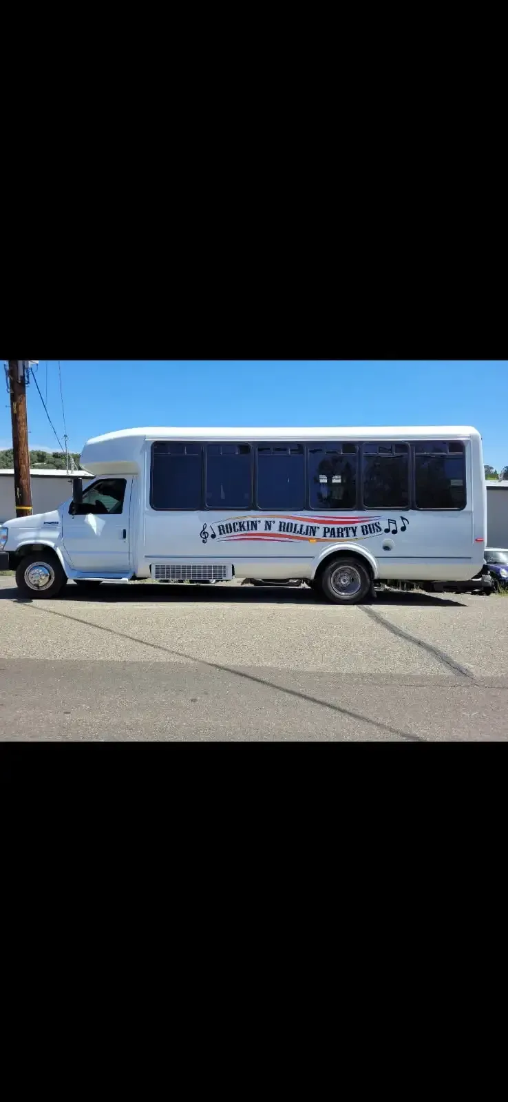 White shuttle bus with tinted windows parked on a sunny street near a palm tree.