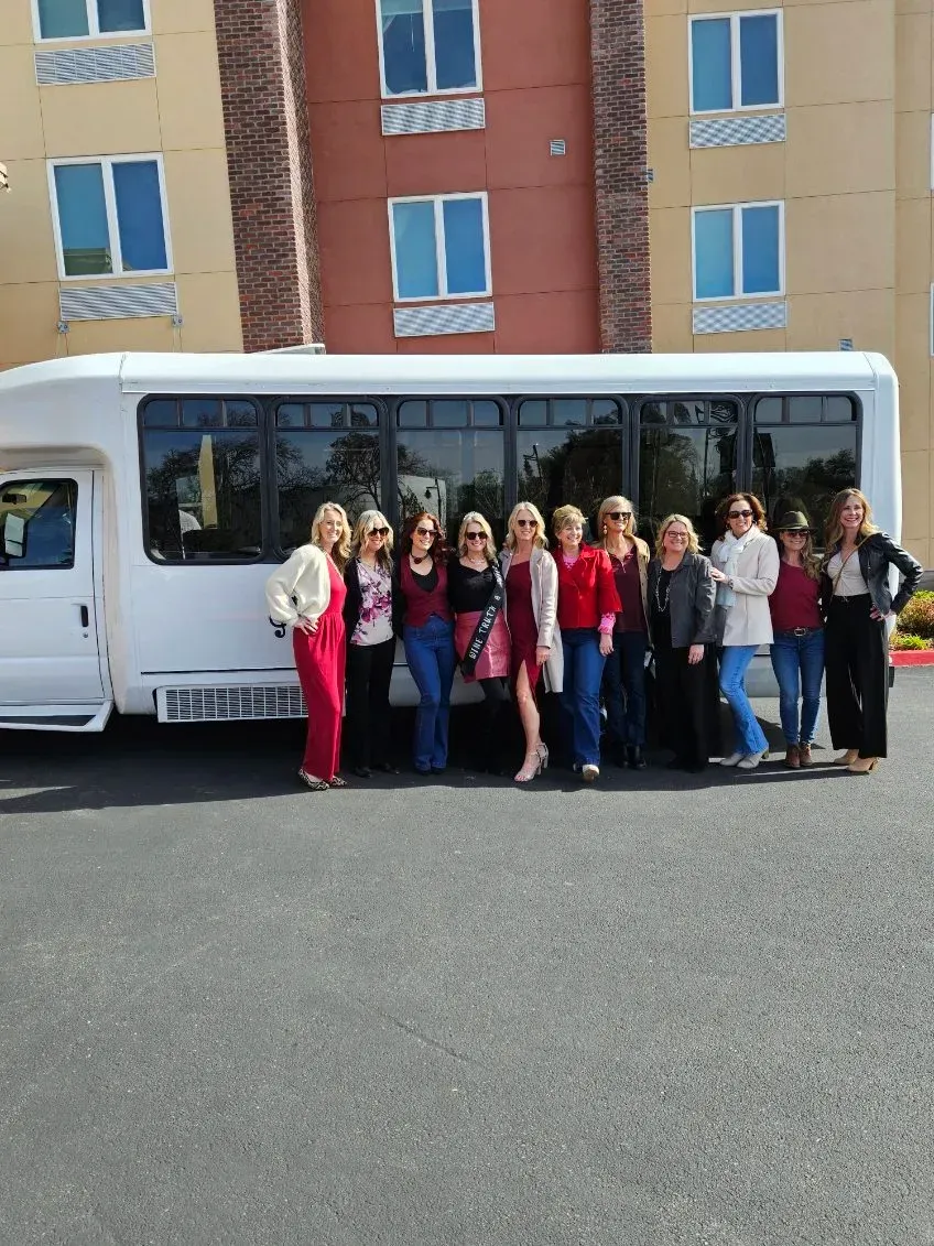 Group of people standing in front of a white bus in a parking lot, with apartment buildings behind them