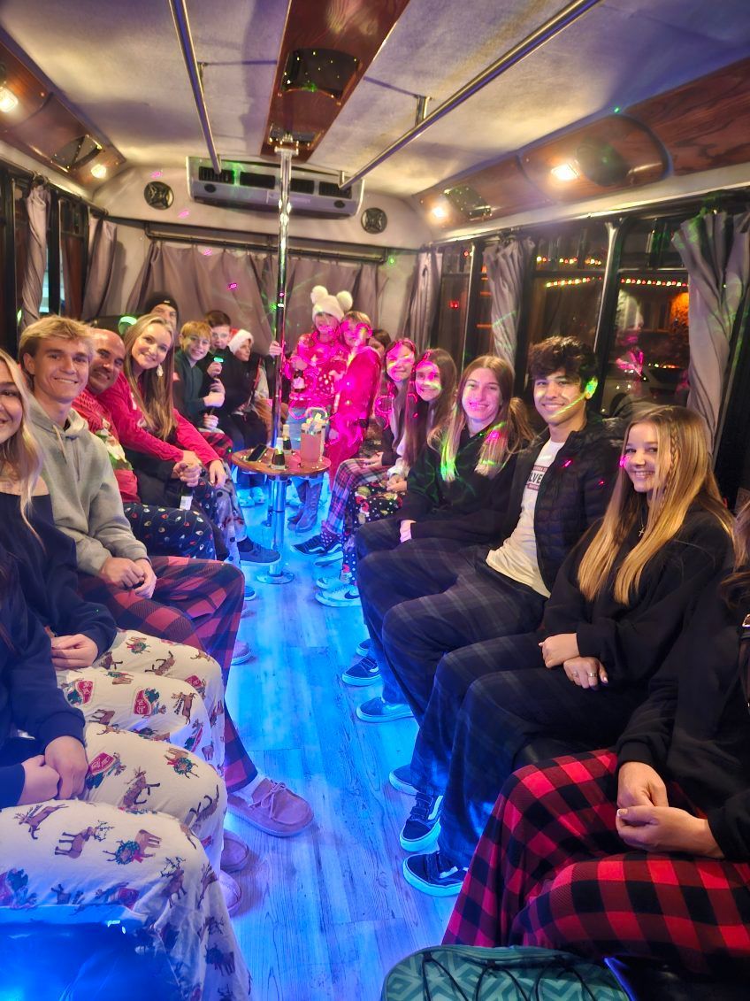 People in colorful costumes posing inside a decorated party bus with purple lighting and balloons