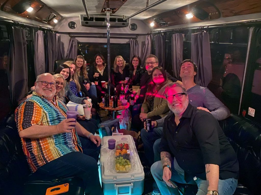 Group posing for a selfie beside a white bus, smiling outdoors under cloudy skies