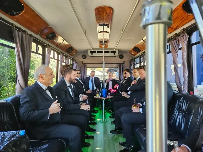 People seated in a bus-like vehicle with black leather seats and green-lit aisle, talking and facing each other