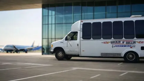 White shuttle van parked beside airport terminal with planes visible in the background