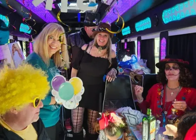 People posing on a decorated party bus with balloons, colorful lights, and festive costumes