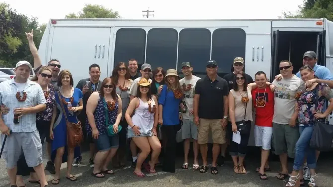 Large group posing in front of a white bus, many wearing patriotic red, white, and blue clothing.