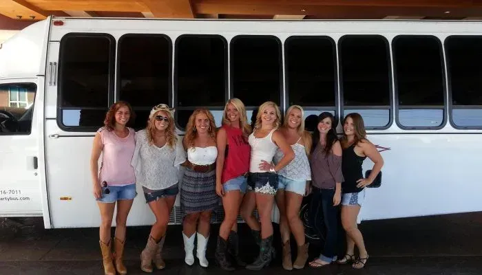 Seven people posing in front of a white bus, smiling at the camera.