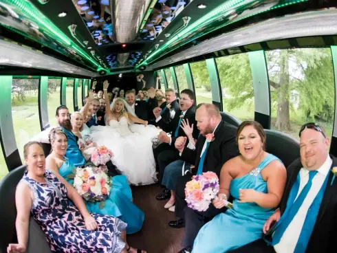 Wedding party celebrating on a bus, with bride in white and guests holding colorful bouquets