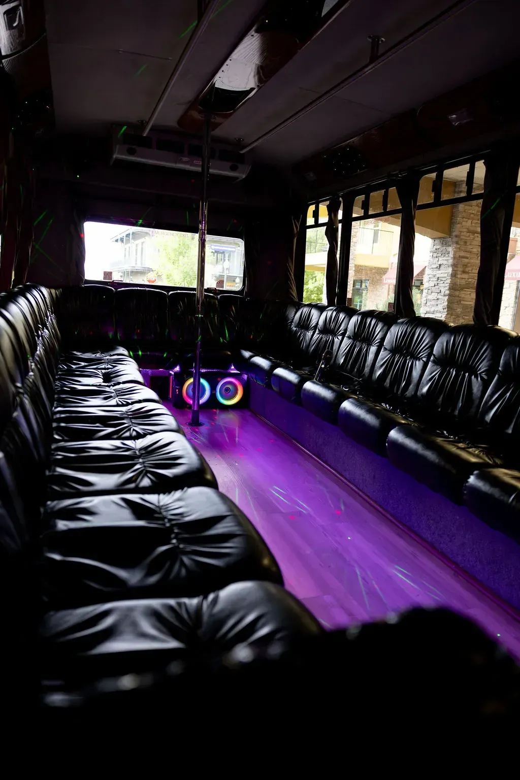 Interior of a party bus with black leather seats, purple floor lighting, and a colorful speaker at the center.