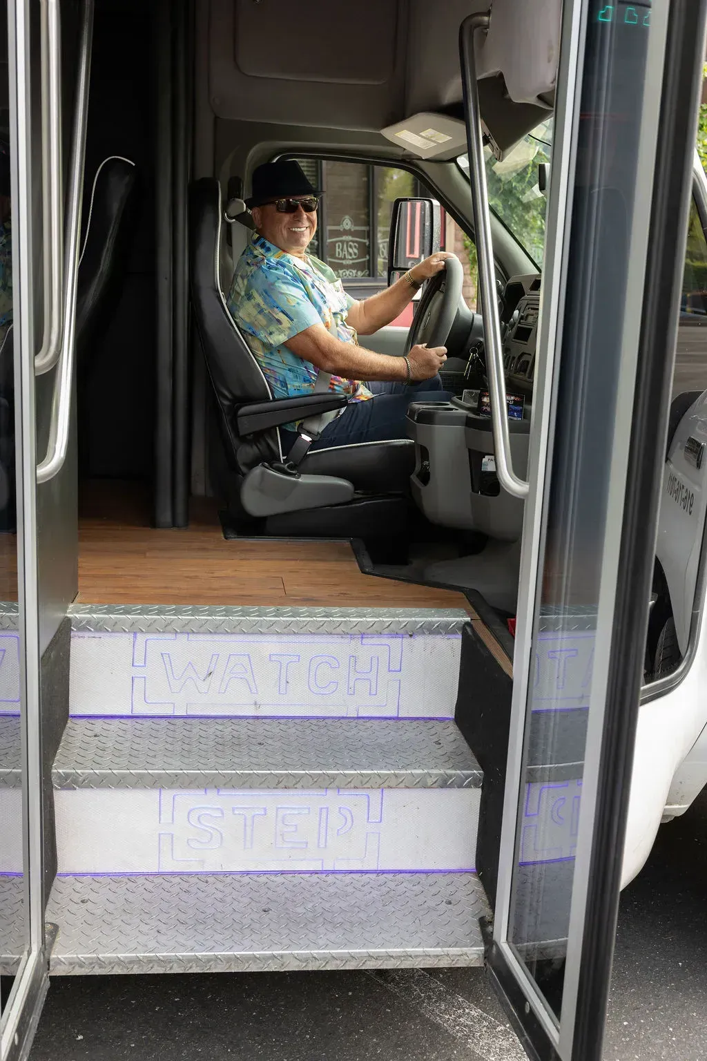 Bus driver seated at the wheel, viewed through the open front door and steps.