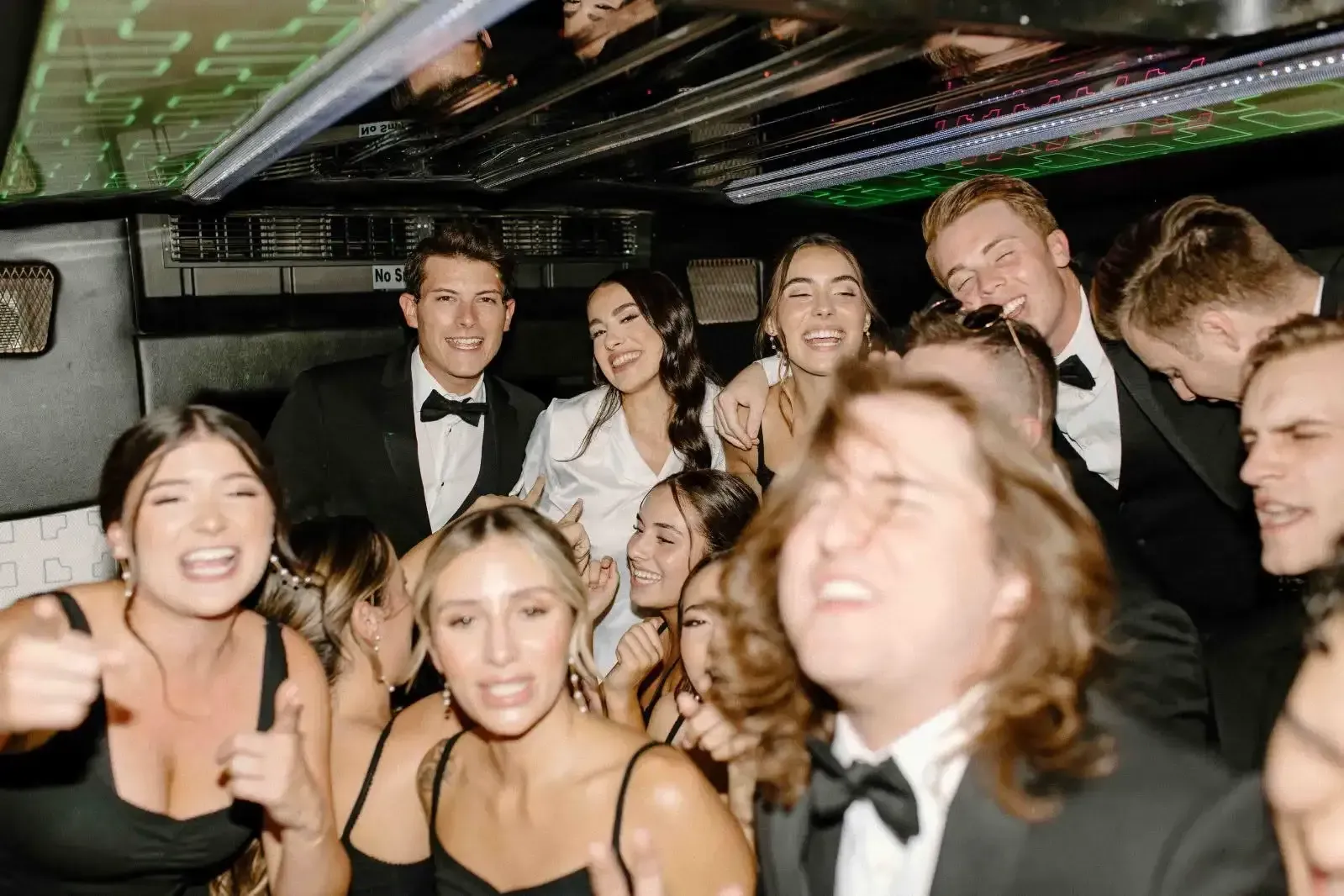 Group of smiling people dressed formally, posing together inside a party bus.