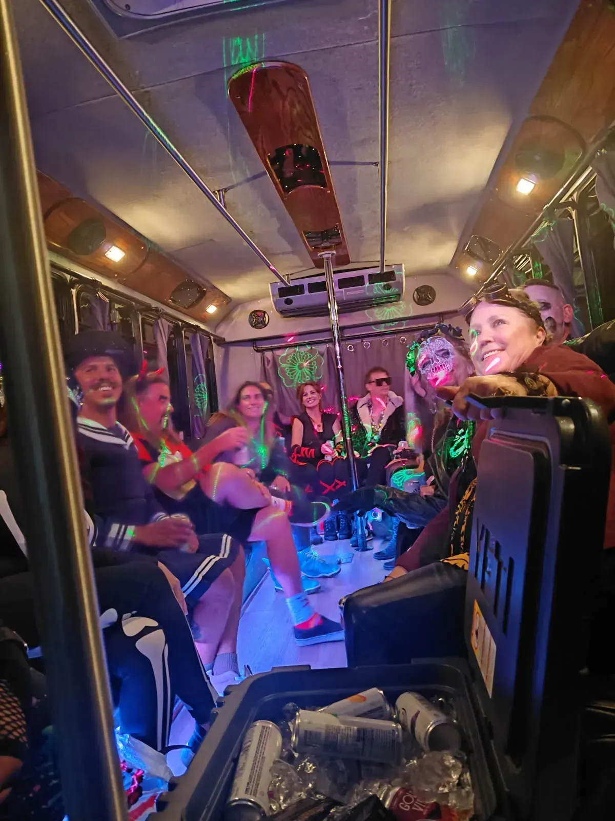 People dancing inside a colorful party bus with neon lights and a smiling driver at the front