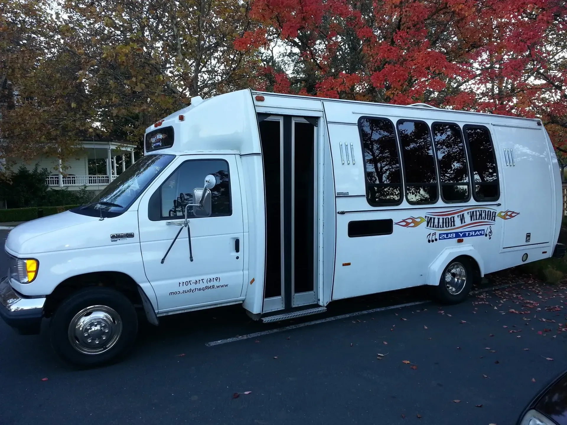White shuttle bus parked on a street in front of autumn trees