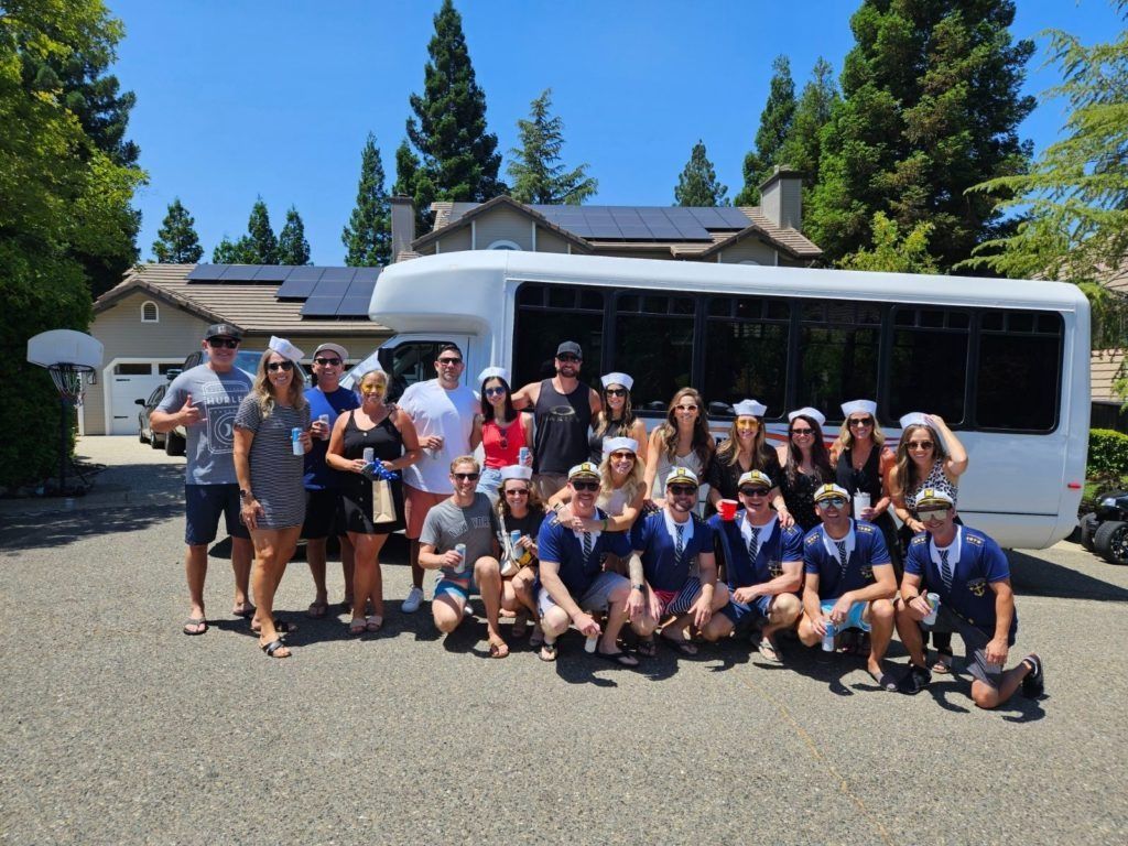 Group of people posing in front of a white shuttle bus on a sunny day outdoors.