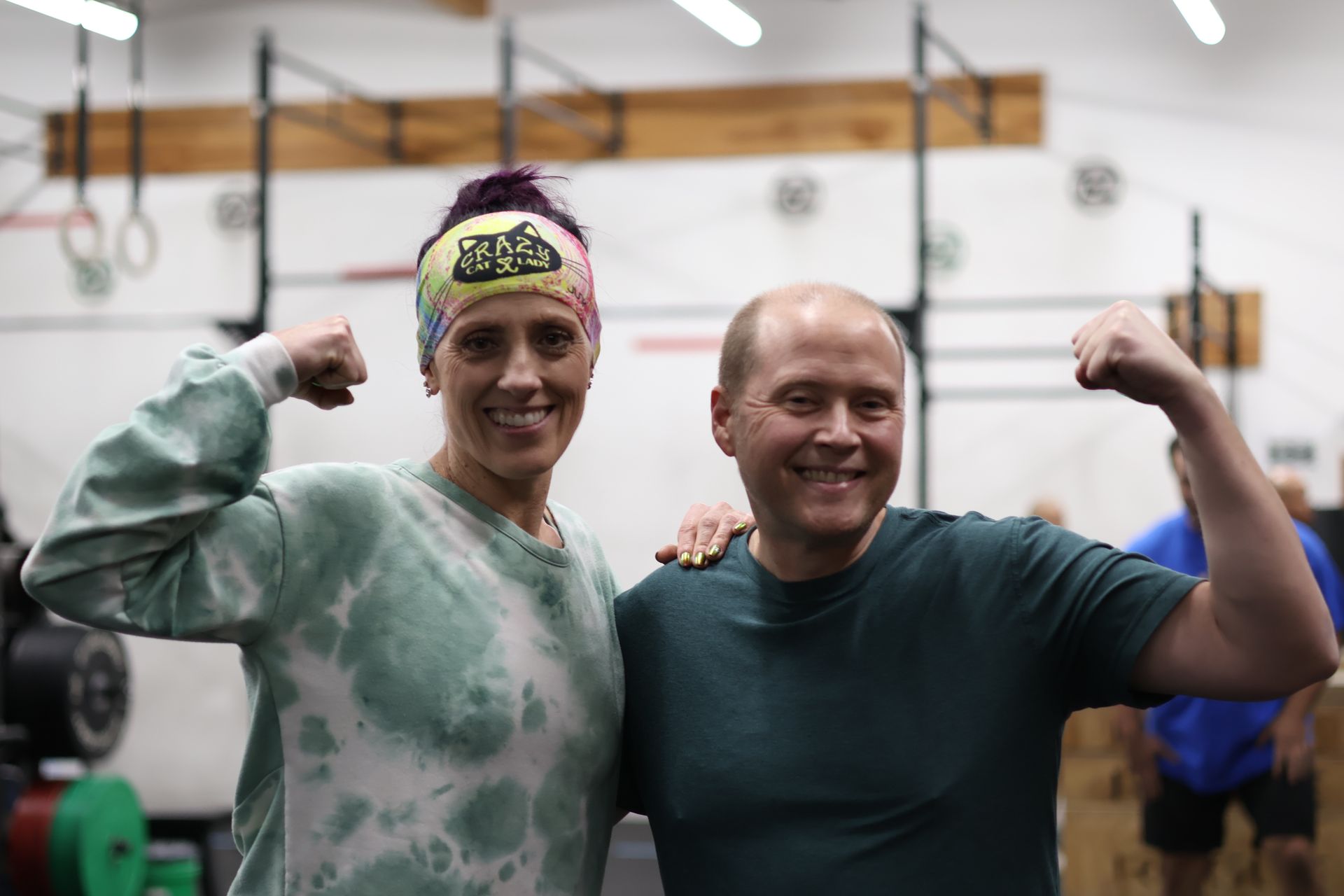 Two smiling people flexing in a gym, standing shoulder to shoulder.