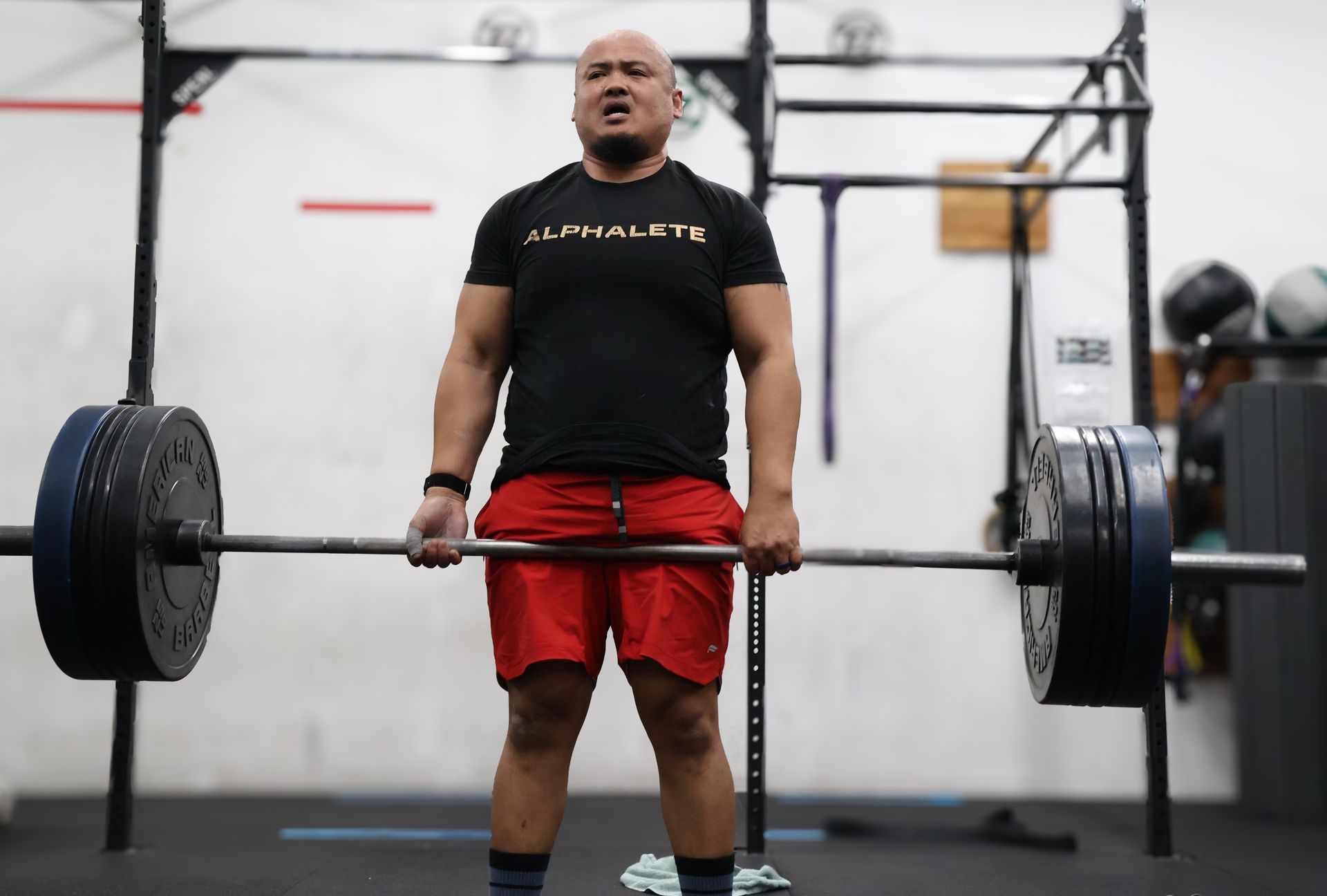 Man deadlifting a heavy barbell in a gym, wearing a black shirt and red shorts.