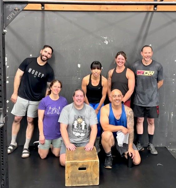 Three men lifting barbells in a CrossFit gym with green wall art and black flooring.