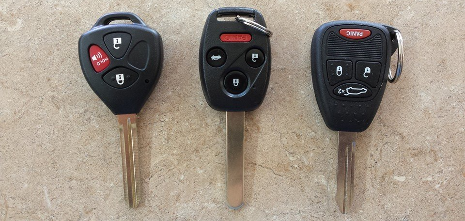 Three black car keys with keychains on a beige surface.