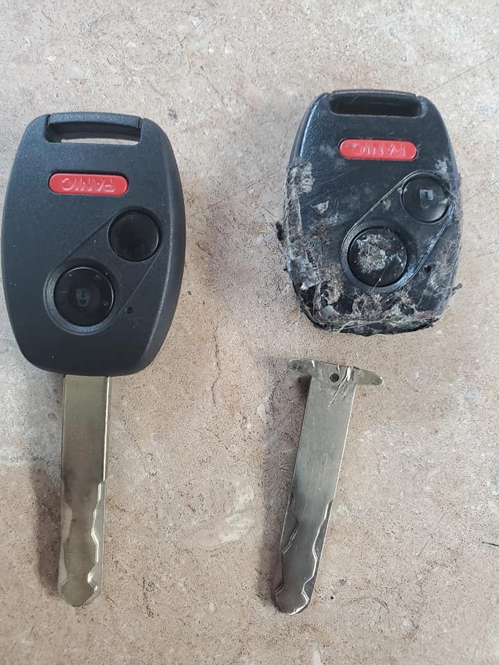 Two black Honda car keys, one new, one old, and a separate key blade, all on a light brown surface.