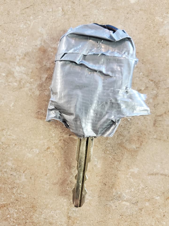 Key wrapped in silver duct tape against a beige patterned background.