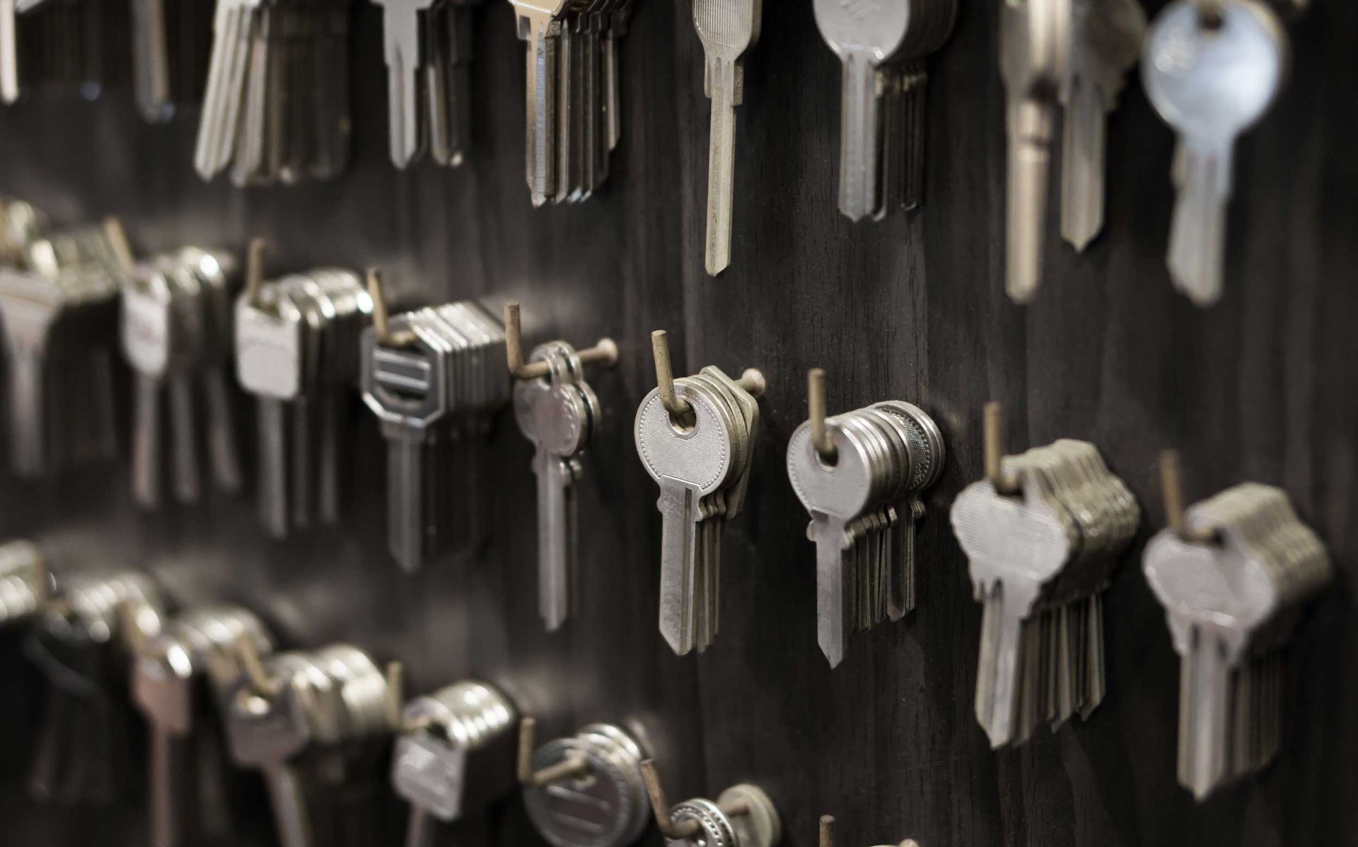 Rows of metal keys hanging on a wall display, organized by size and shape in a locksmith shop. Rows of metal keys hanging on a wall display, organized by size and shape in a locksmith shop.