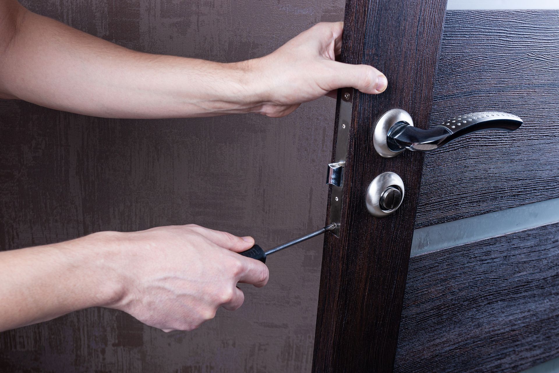 Man with screwdriver installs door lock, showcasing locksmith skills for home security. Man with screwdriver installs door lock, showcasing locksmith skills for home security.