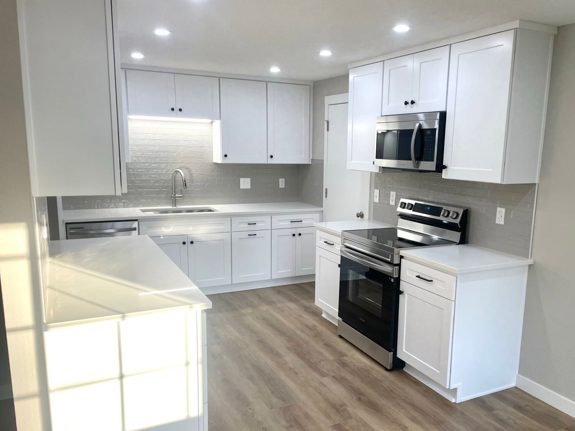 Bright modern white kitchen with stainless steel appliances and wood flooring