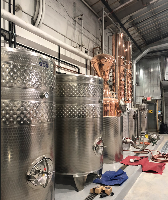 A row of stainless steel tanks are lined up in a warehouse