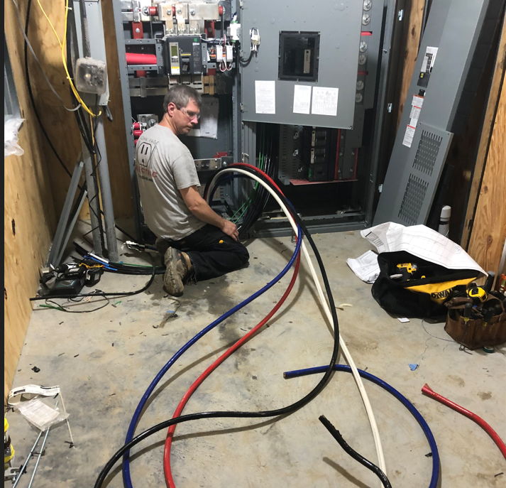 A man is kneeling on the floor working on electrical wires