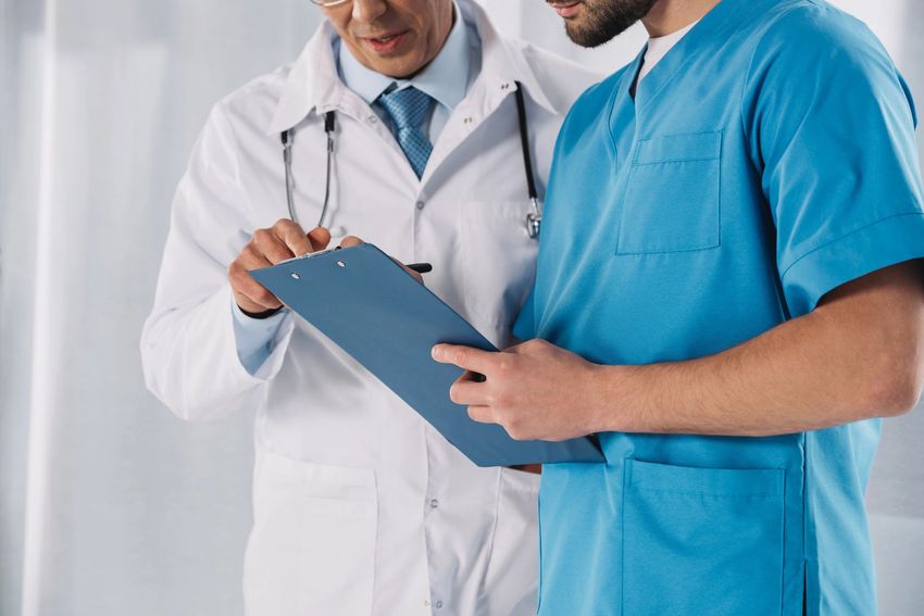 Un médico y una enfermera con uniformes quirúrgicos revisan juntos unas notas en un portapapeles.