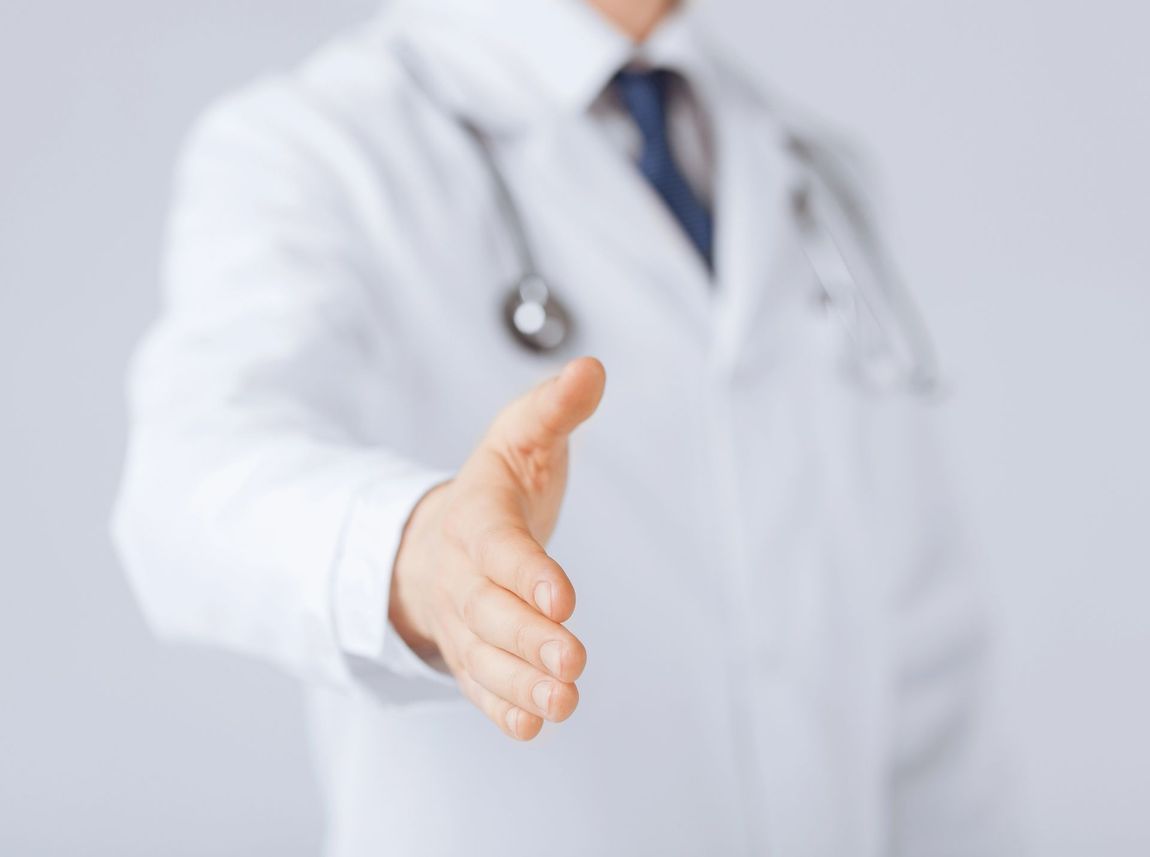 Médico con bata blanca extendiendo la mano para estrecharla.