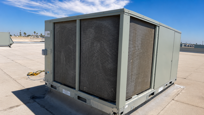 Large gray rooftop HVAC unit with black mesh intake panels on a sunlit flat roof