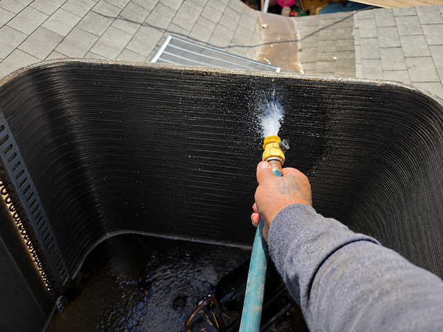 Hand spraying water onto a black textured hot tub or pool wall with a hose outdoors