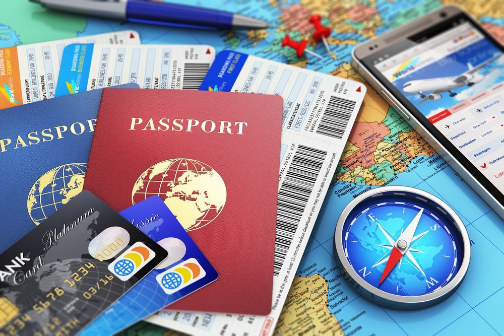 Pasaporte, billetes, tarjetas de crédito, brújula, teléfono inteligente con aplicación de viajes, bolígrafo y chinchetas en un mapa.