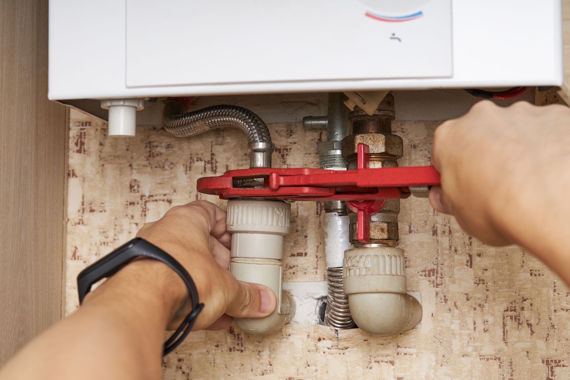 Person using a wrench to tighten plumbing connections near a water heater. Person using a wrench to tighten plumbing connections near a water heater.