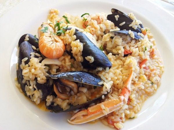 Riso ai frutti di mare con cozze, gamberi e verdure miste su un piatto bianco.
