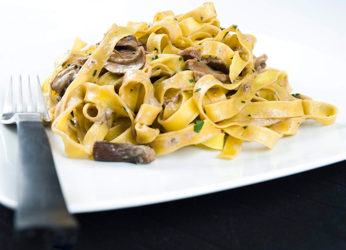 Piatto di fettuccine con funghi e salsa cremosa su un piatto bianco.
