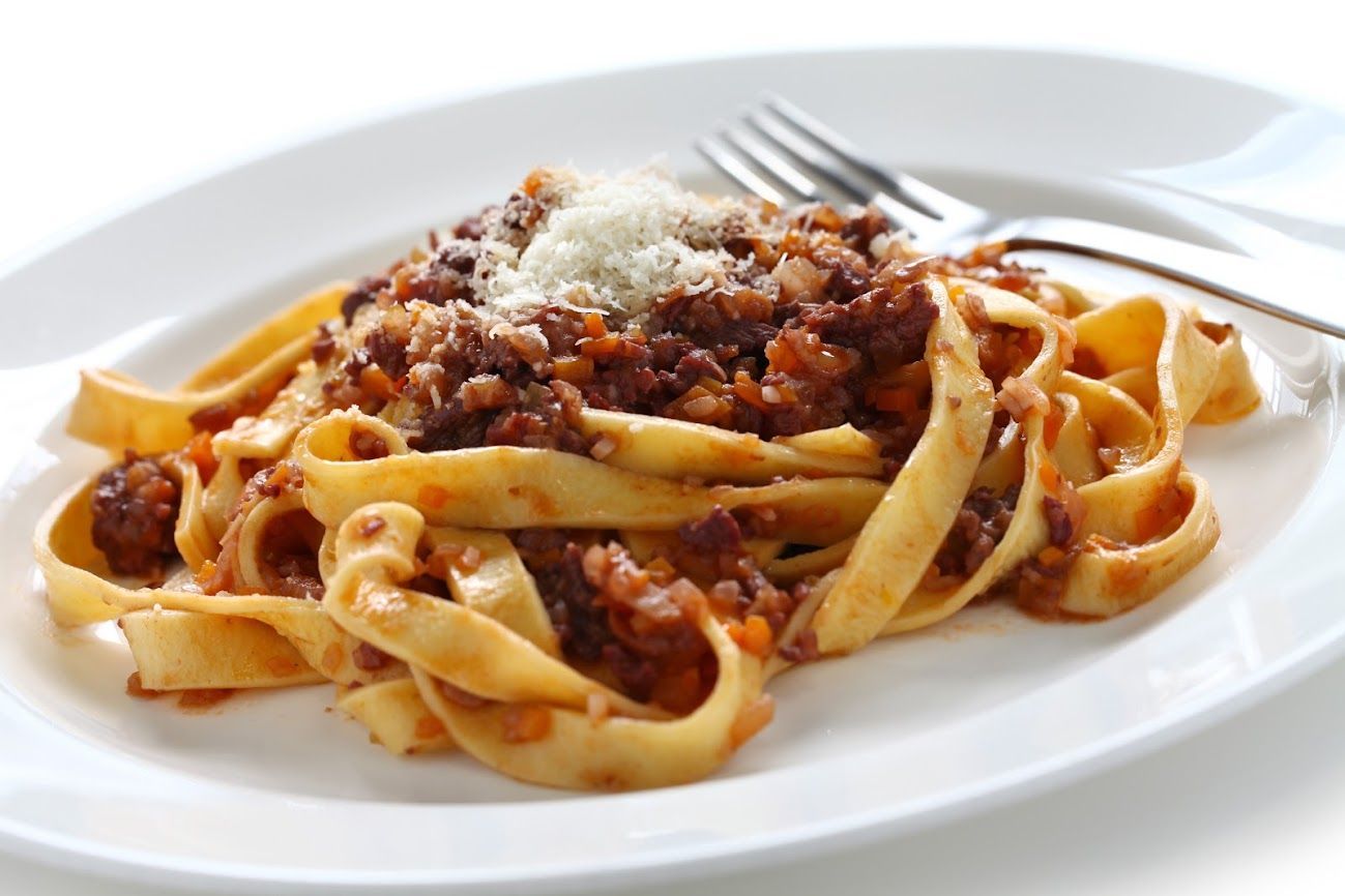 Fettuccine al ragù e formaggio grattugiato su un piatto bianco.