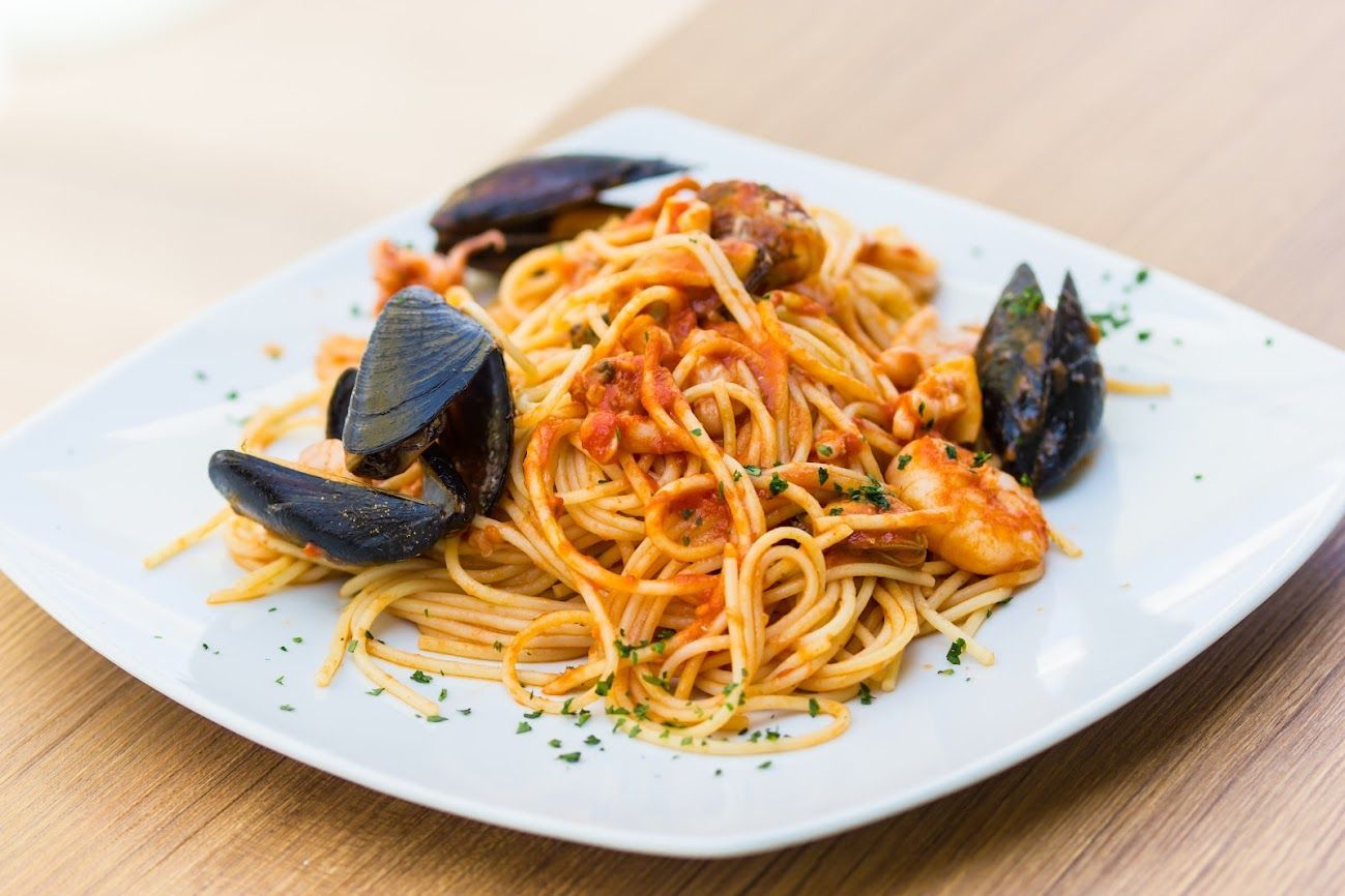 Piatto di spaghetti con cozze e salsa di pomodoro su un piatto quadrato bianco.