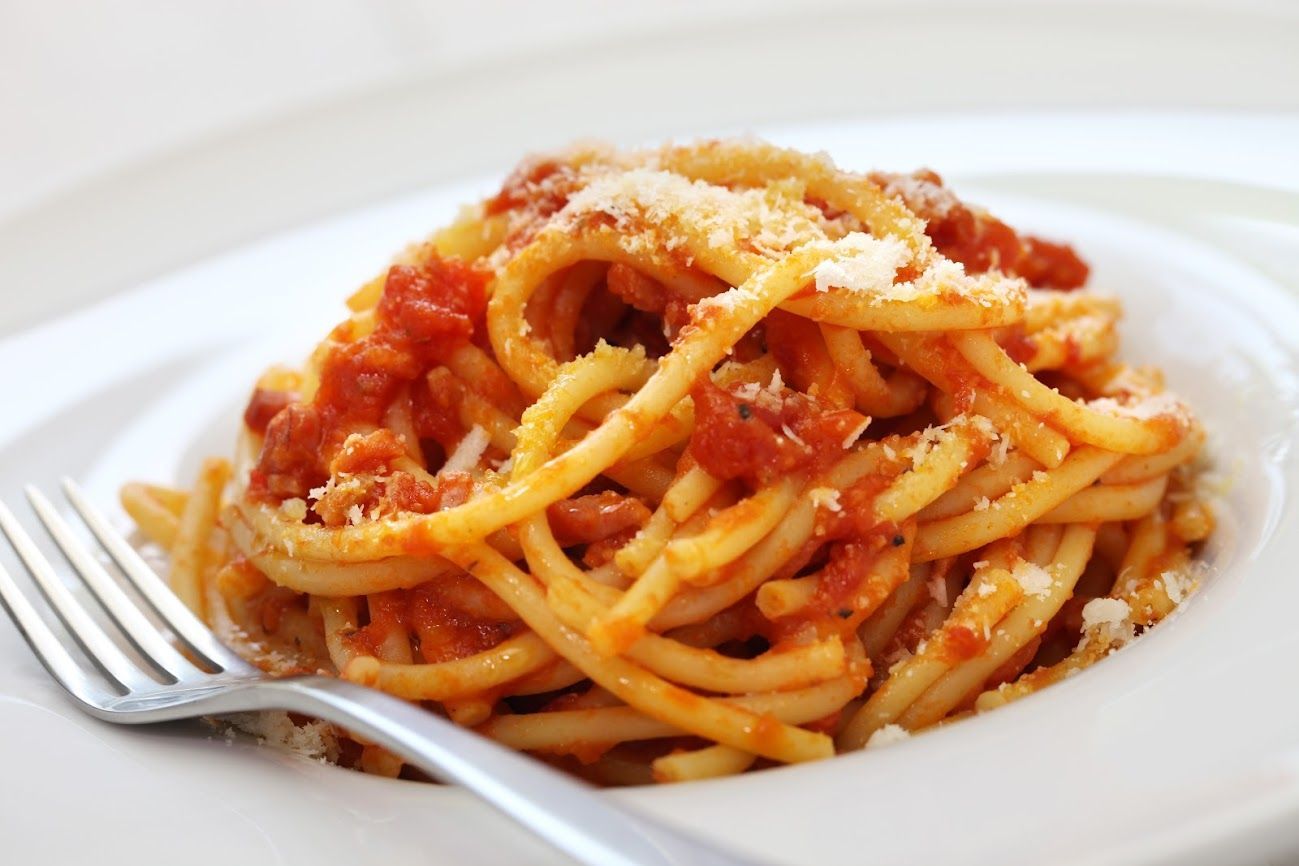 Piatto di spaghetti al sugo di pomodoro e formaggio grattugiato, con forchetta a parte.