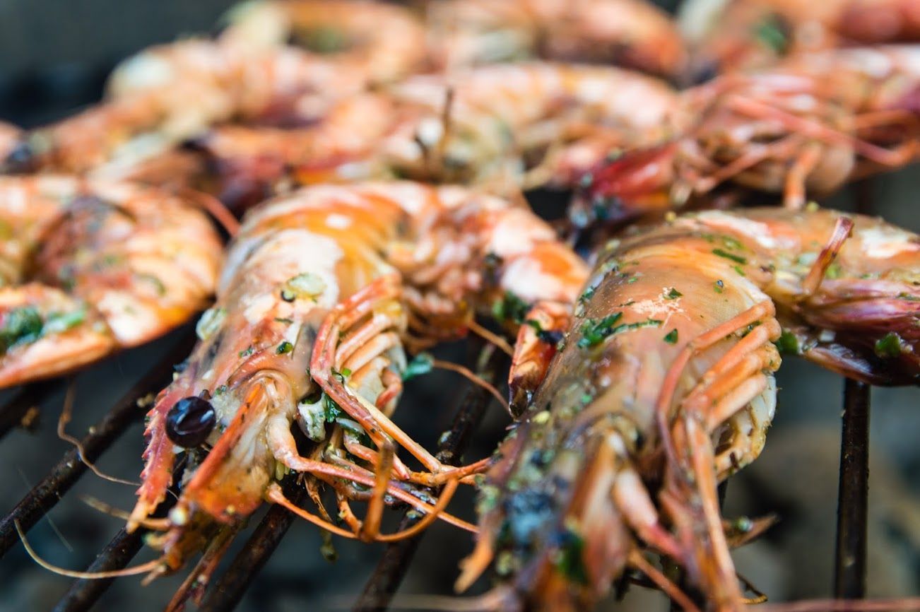 Spiedini di gamberi grigliati con gusci d'arancia ed erbe aromatiche, disposti su una griglia per barbecue.