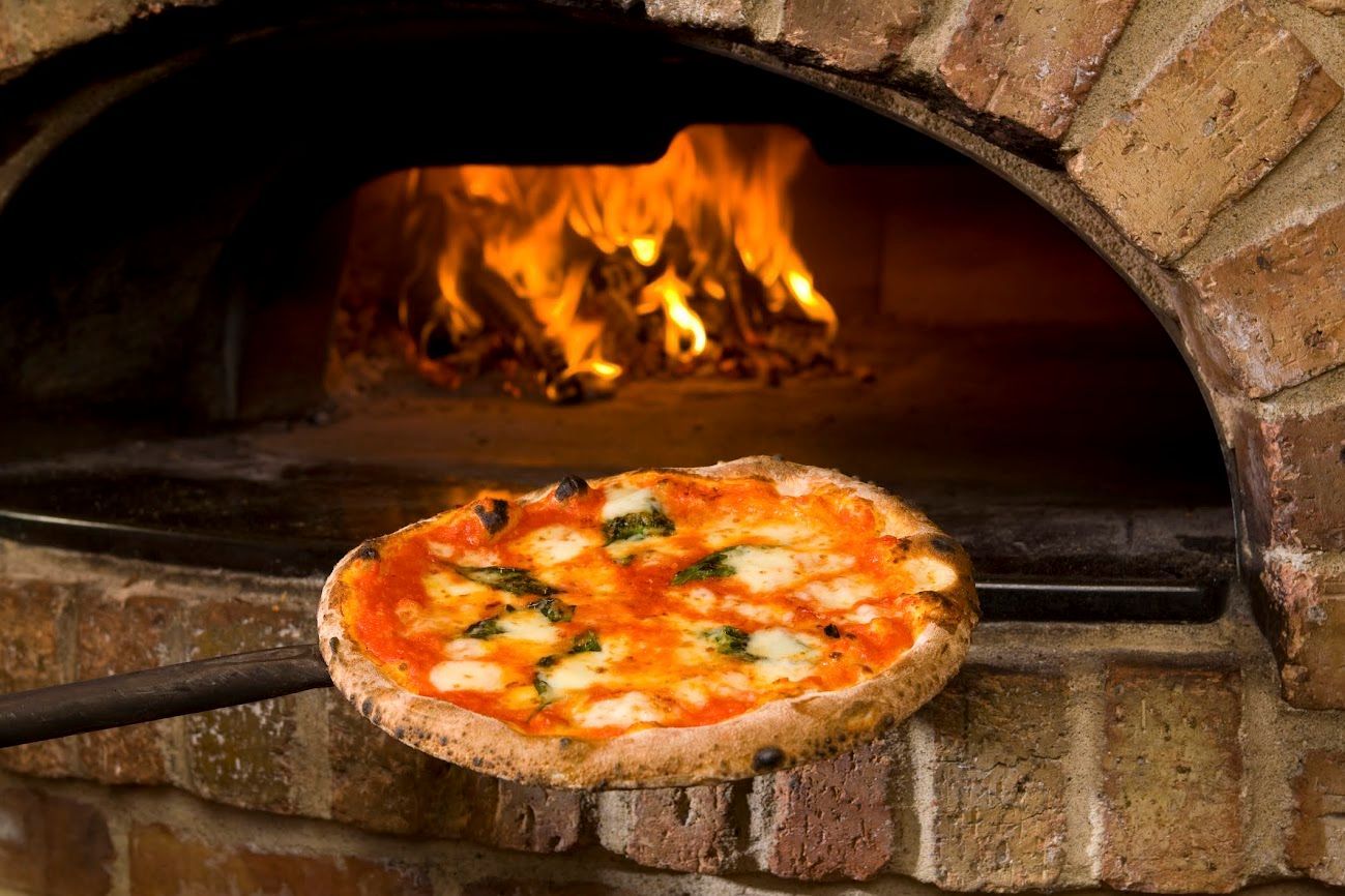 Pizza che cuoce in un forno a legna, con le fiamme che brillano alle sue spalle.