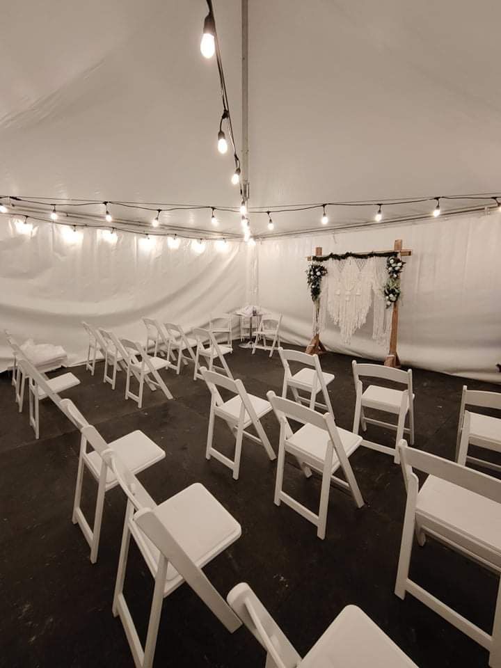 Une rangée de chaises pliantes blanches est alignée dans une tente.