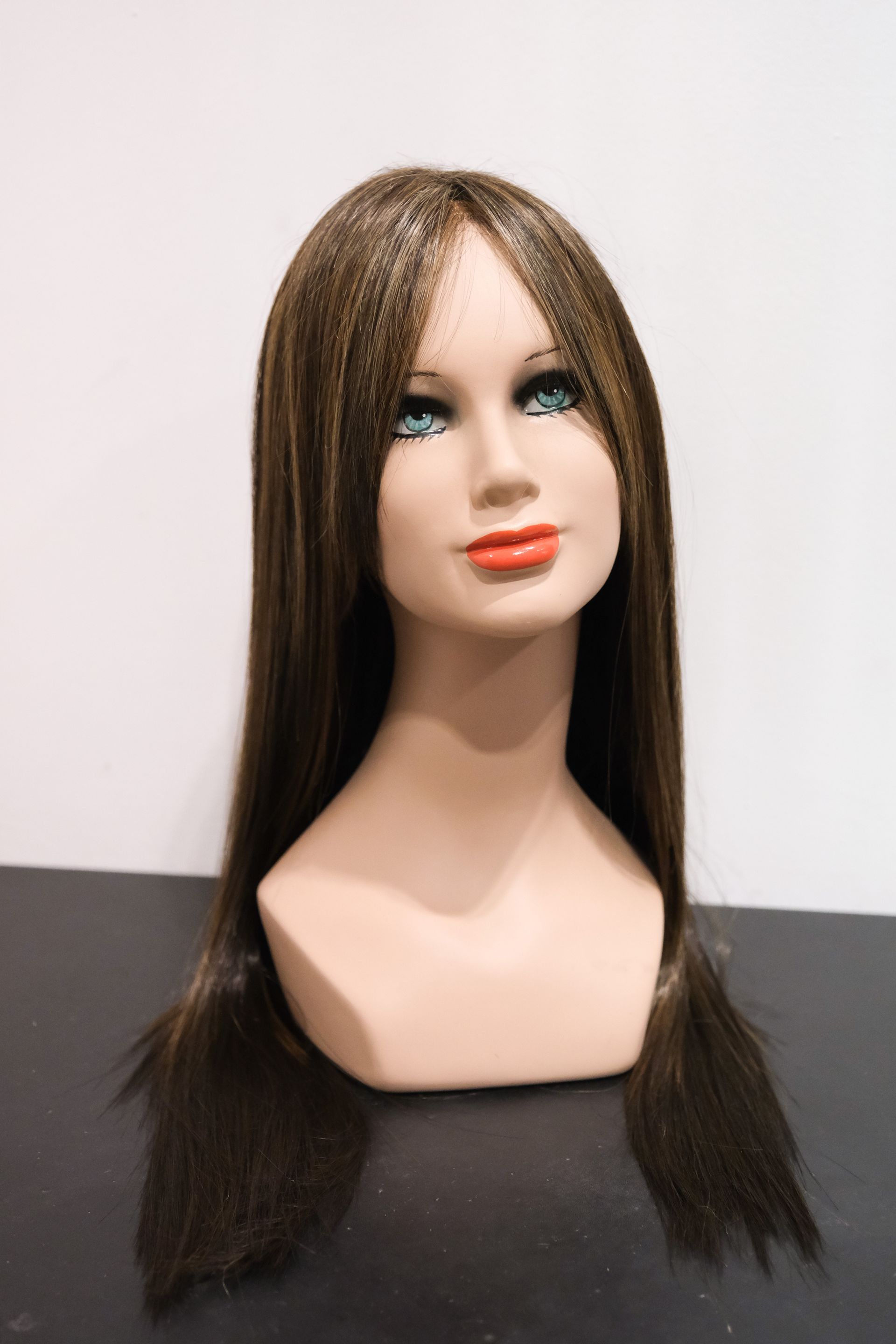 Testa di manichino con parrucca marrone, capelli lunghi e lisci e rossetto rosso.