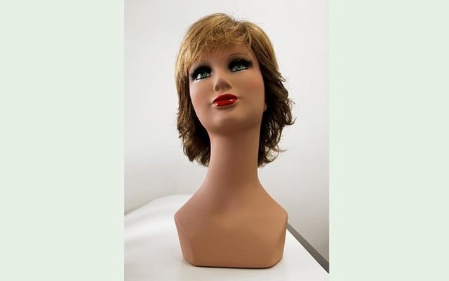 Testa di manichino con parrucca lunga fino alle spalle; carnagione abbronzata, rossetto rosso.