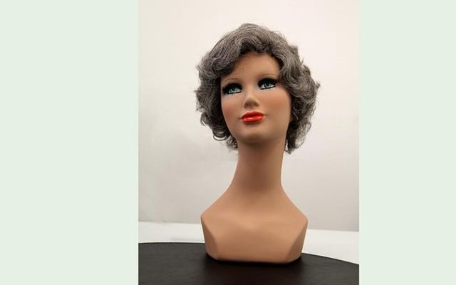 Testa di manichino con parrucca corta, grigia e ondulata e rossetto rosso.