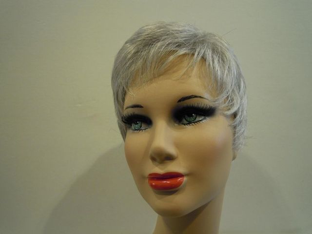 Testa di manichino con capelli corti e argentati, labbra rosse e trucco scuro sugli occhi.