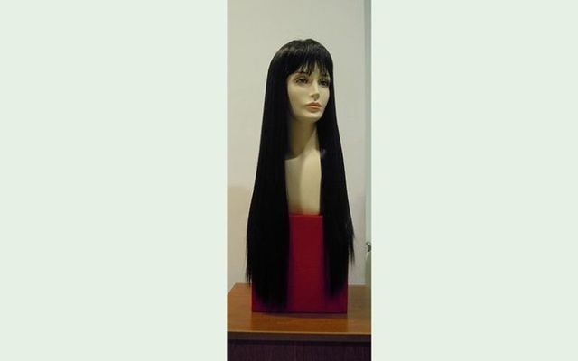 Una parrucca nera con capelli lunghi e lisci e frangia su una testa di manichino, esposta su una scatola rossa.